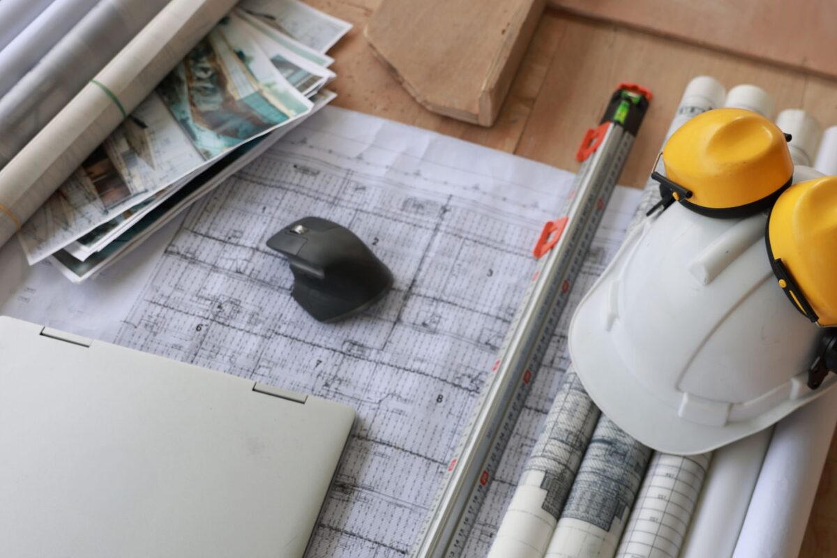 Work desk with architectural plans, a mouse, and a hard hat.